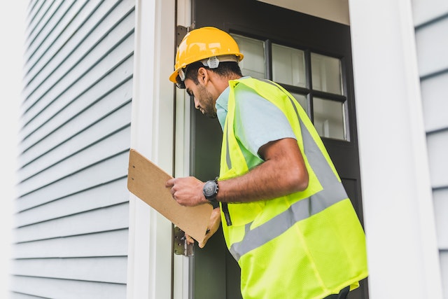 a-contractor-in-a-yellow-vest-inspects-the-front-door-of-a-rental-property-to-ensure-it-adheres-to-building-codes