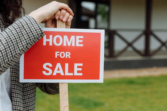 person-leaning-on-home-for-sale-sign